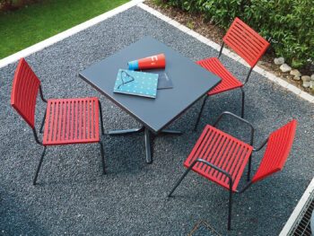 Moderner Schaffner-Tisch Schaffhausen mit roten Lamello Stühlen im Garten.